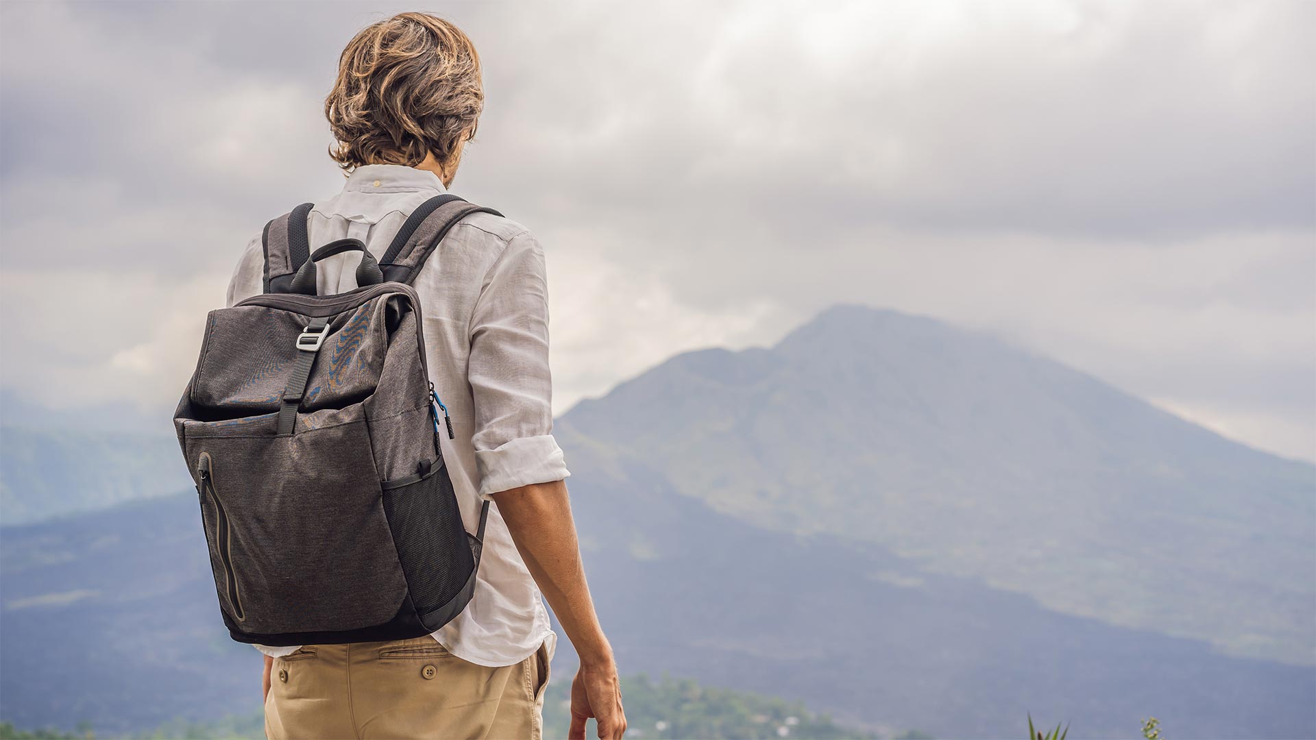 Joven de espaldas con una mochila mirando una montañas
